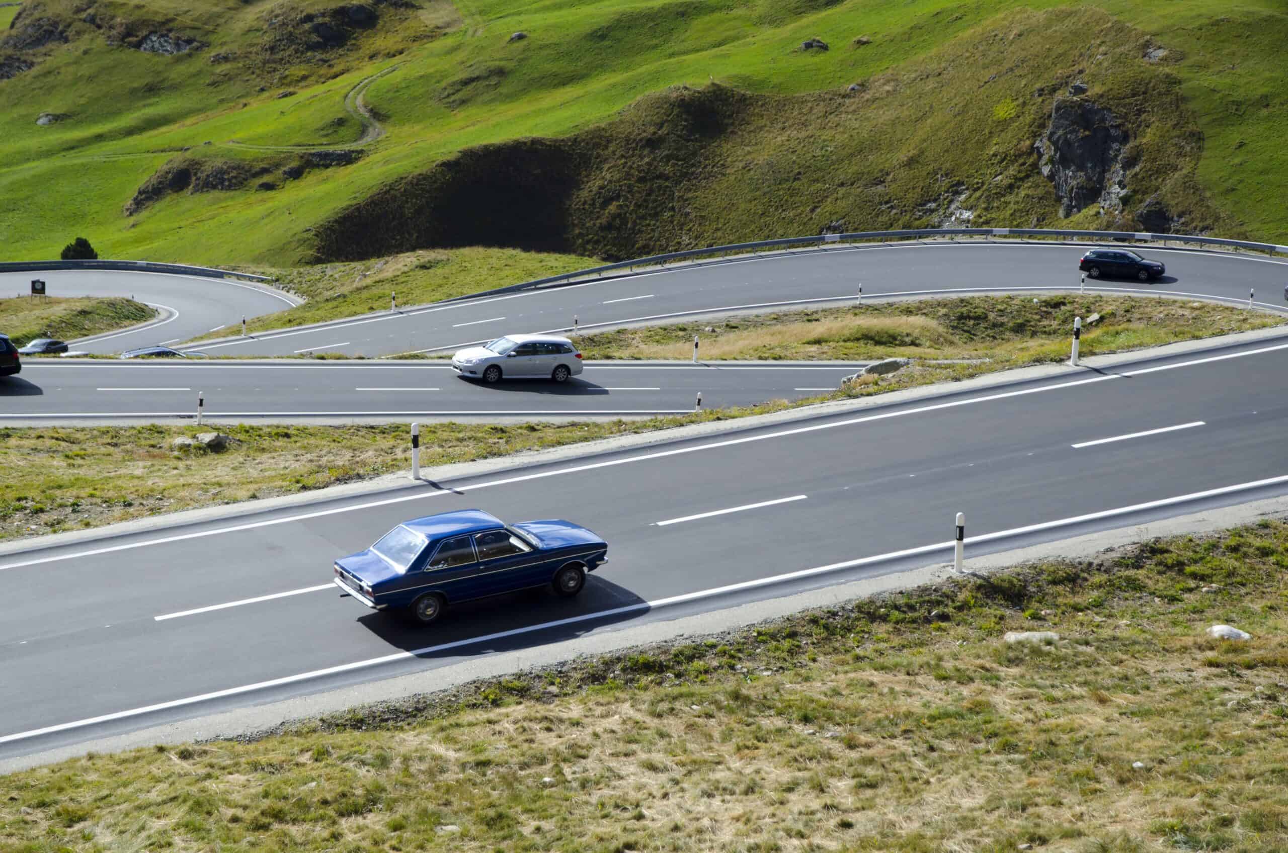 High angle view of cars on the curvy road surrounded by hills covered in greenery in Switzerland